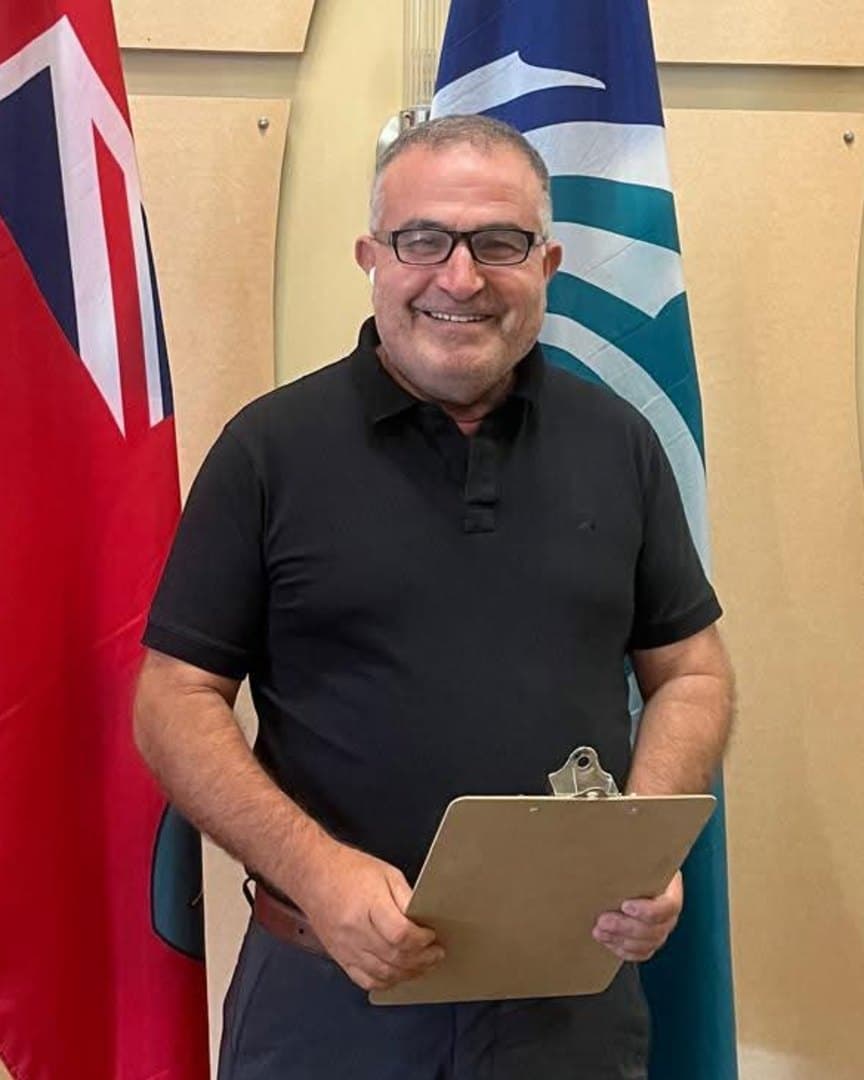 Ahmed Alsabaawi, candidate for City Councillor in Ward 24, Barrhaven East, holding a clipboard in front of the Ontario, City of Ottawa and Algonquin Anishinàbeg flags