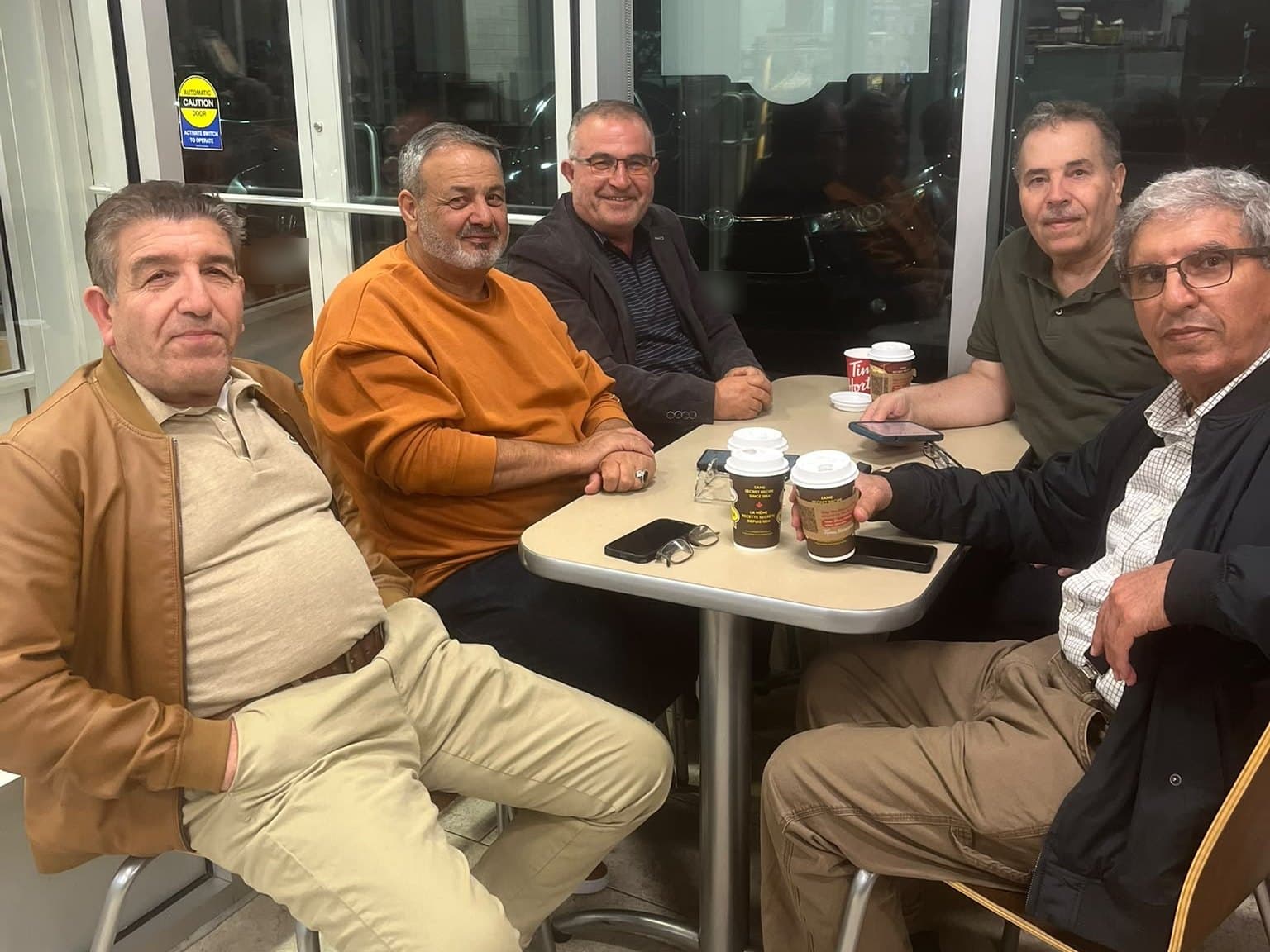 Ahmed Alsabaawi and four other men around a table at Tim Hortons in the evening, coffee cups in front of them