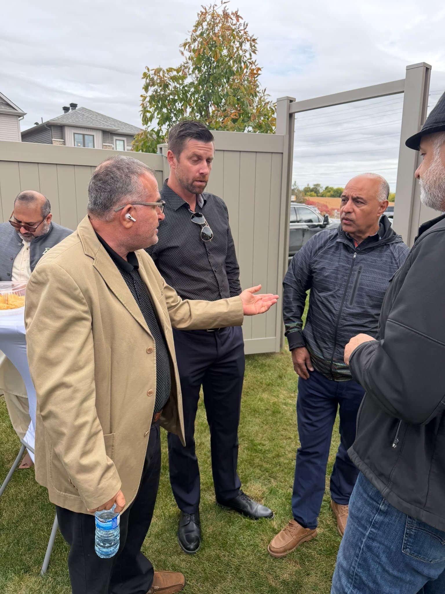 Ahmed Alsabaawi, in a tan jacket, talking with three men on the lawn at a backyard gathering