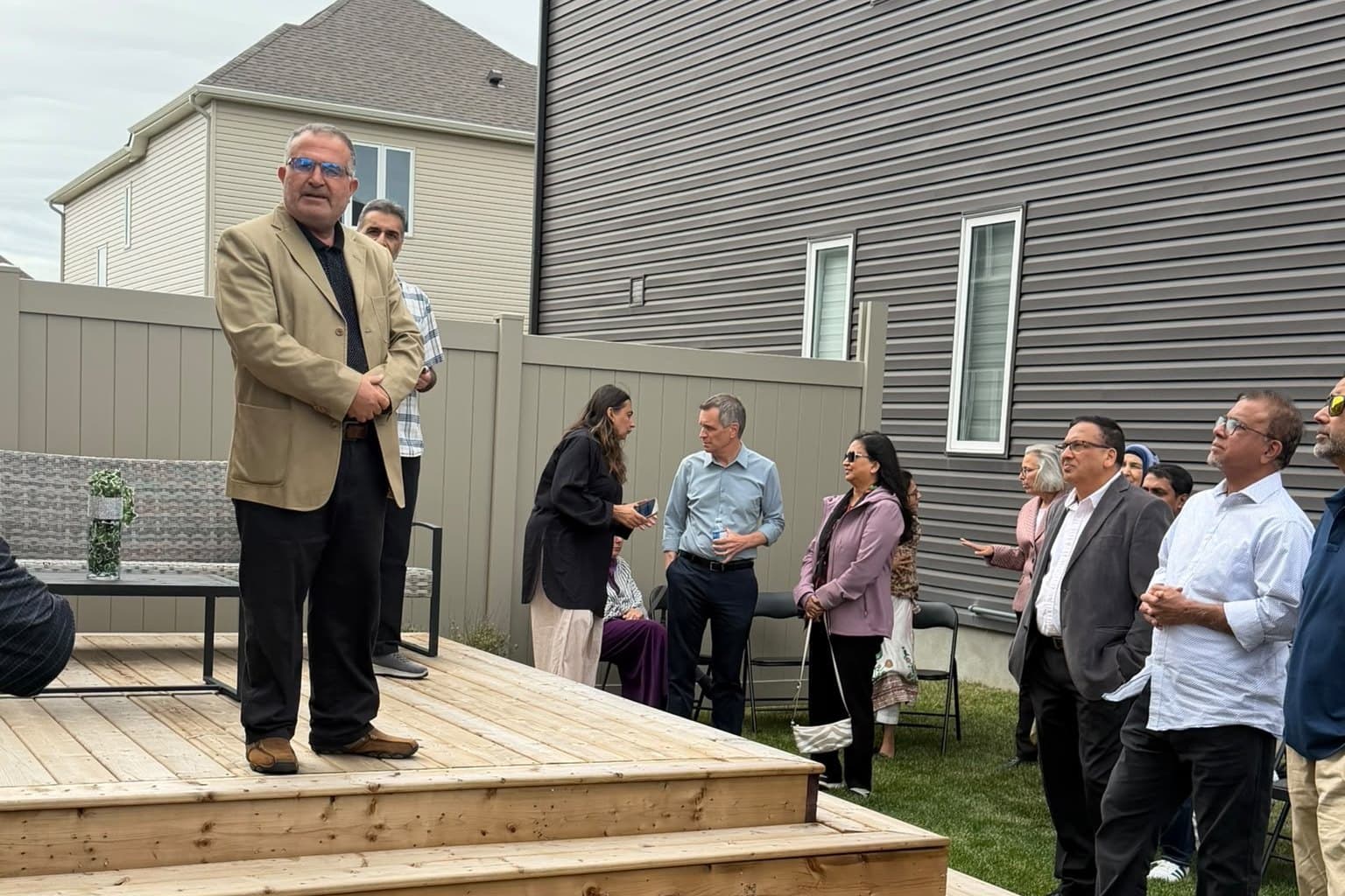 Ahmed Alsabaawi standing on a backyard deck, speaking to people gathered on the lawn